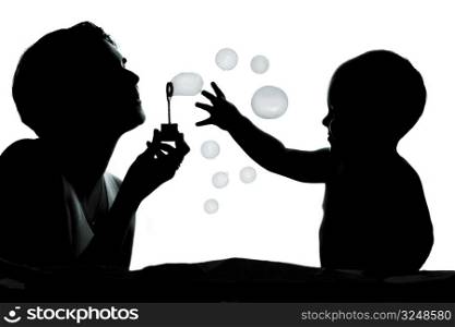 1 year old baby and his mother are playing together with bubbles. They are silhouetted.
