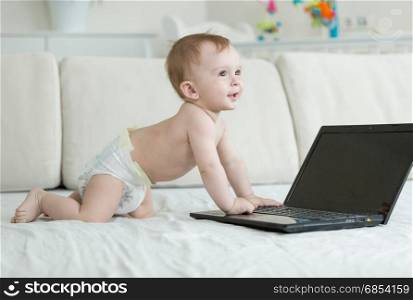 1 year old baby boy in diapers crawling and reaching for laptop