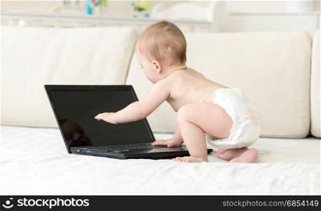 1 year old baby boy on bed using laptop