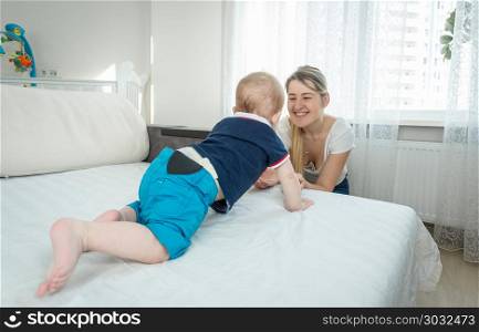 10 months old baby boy crawling on bed towards smiling young mother. 10 months old baby boy crawling on bed towards smiling mother