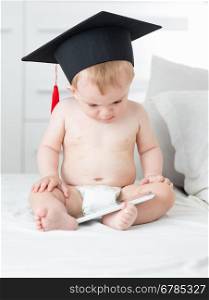 10 months old baby boy in diapers wearing graduation cap and using tablet pc