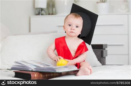 10 months old baby boy in graduation cap sitting on sofa with books
