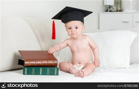 10 months old baby boy in mortarboard hat sitting with stack of books