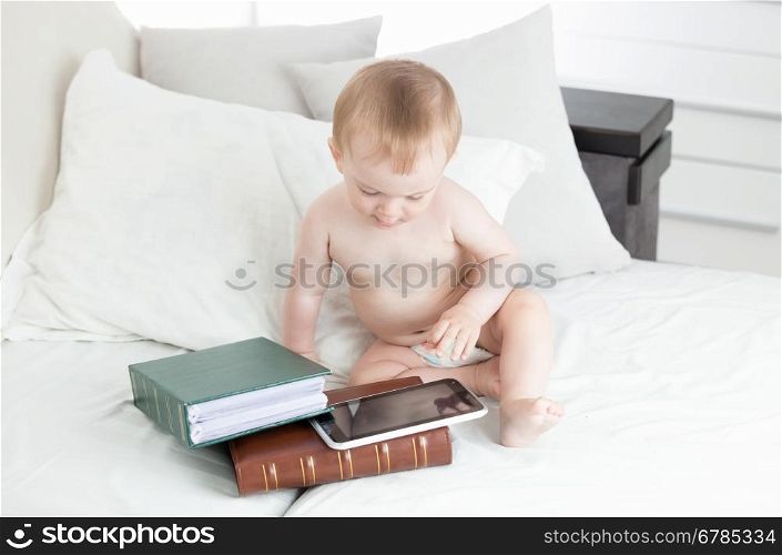 10 months old baby boy sitting next to stack of books and using digital tablet