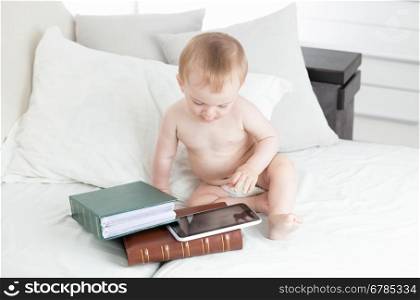 10 months old baby boy sitting next to stack of books and using digital tablet