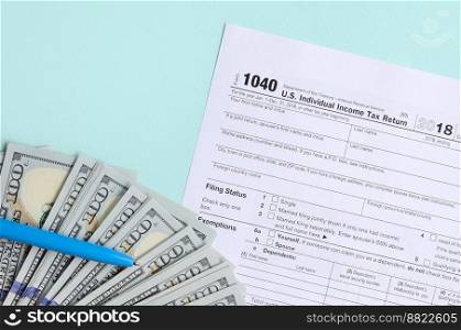 1040 tax form lies near hundred dollar bills and blue pen on a light blue background. US Individual income tax return.. 1040 tax form lies near hundred dollar bills and blue pen on a light blue background. US Individual income tax return