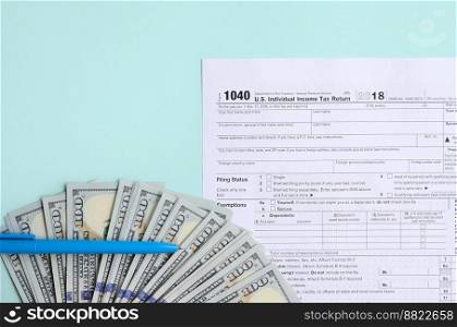 1040 tax form lies near hundred dollar bills and blue pen on a light blue background. US Individual income tax return.. 1040 tax form lies near hundred dollar bills and blue pen on a light blue background. US Individual income tax return