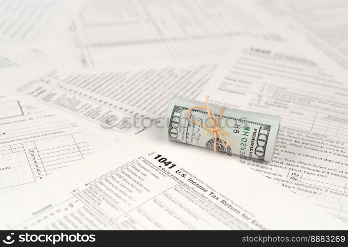 1041 U.S. Income tax return for Estates and Trusts form with roll of american dollar banknotes close up. Concept of tax period in United States. 1041 U.S. Income tax return for Estates and Trusts form with roll of american dollar banknotes