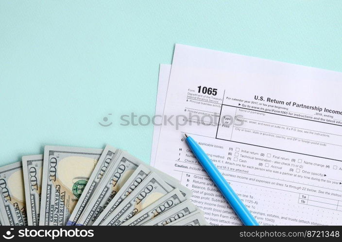 1065 tax form lies near hundred dollar bills and blue pen on a light blue background. US Return for parentship income.. 1065 tax form lies near hundred dollar bills and blue pen on a light blue background. US Return for parentship income