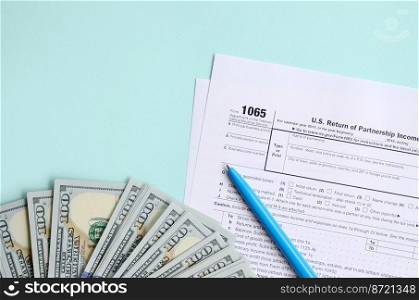 1065 tax form lies near hundred dollar bills and blue pen on a light blue background. US Return for parentship income.. 1065 tax form lies near hundred dollar bills and blue pen on a light blue background. US Return for parentship income