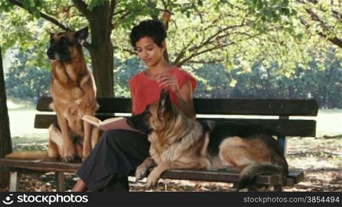11of15 Young people and pet, portrait of happy young latina woman working as dog sitter with german shepherd dogs in park, reading book and relaxing