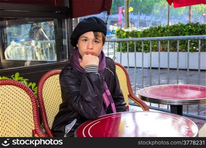 13 year old teenager in a French beret and scarf sitting at a table Parisian cafe on the Champs Elysees