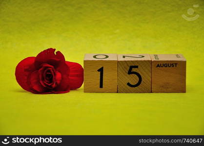 15 August on wooden blocks with a red flower on a yellow background