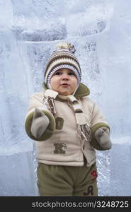 18 months old baby wearing warm clothing at winter and standing in front of a huge ice cube.