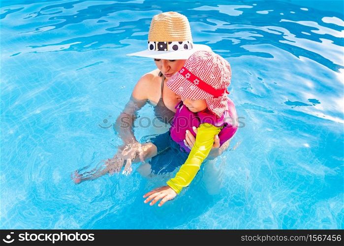 2-3 years old child with mother in swimming pool learn to swim. Baby in swimming west and red hat.Summer at home concept. Above shoot. 2-3 years old child with mother in swimming pool learn to swim. Summer at home concept.