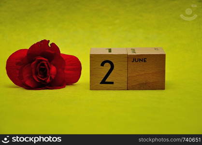 2 June on wooden blocks with a red flower on a yellow background