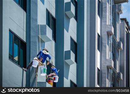 2 painters are hanging on ropes and harnesses paint the exterior of building.