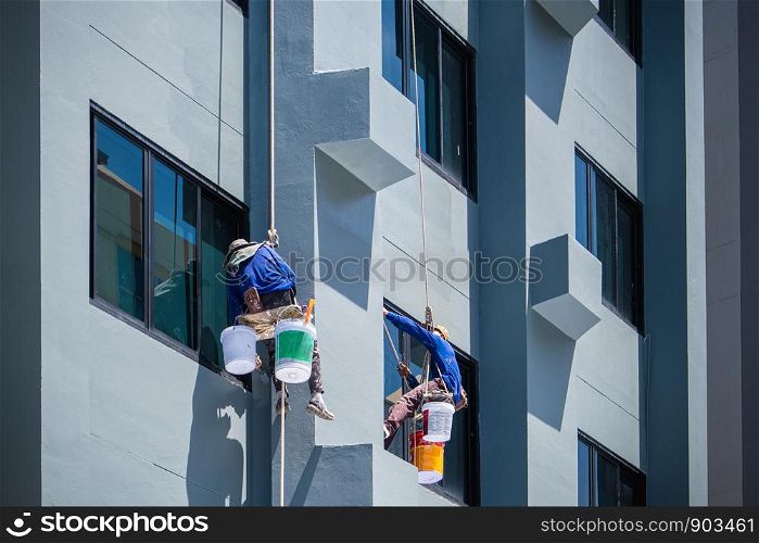 2 painters are hanging on ropes and harnesses paint the exterior of building.