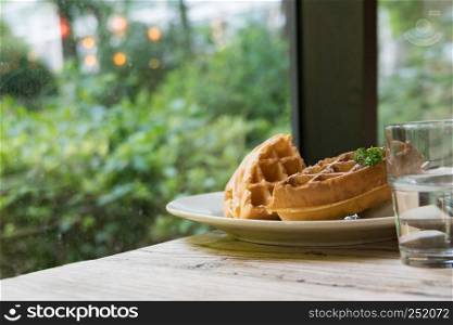 2 pieces of waffle with a glass of water on the wooden table - apply filter