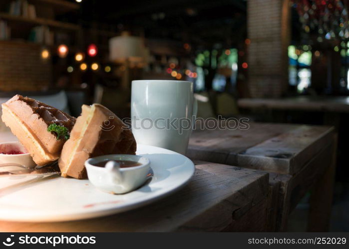 2 pieces of waffle with a white cup of coffee on the wooden table