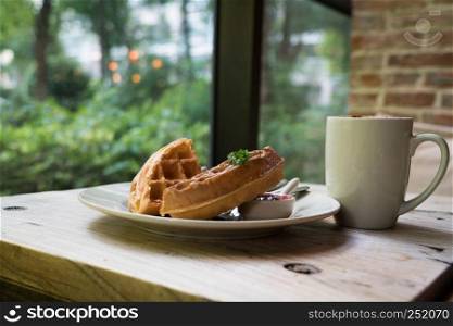 2 pieces of waffle with a white cup of coffee on the wooden table