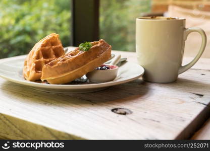 2 pieces of waffle with a white cup of coffee on the wooden table