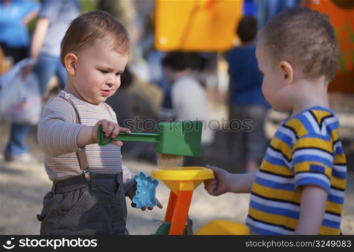 2 years old children are playing together in the sandbox