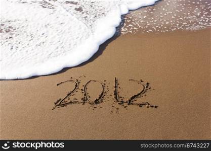 2012 written in sand on beach with sea waves starting to erase the word