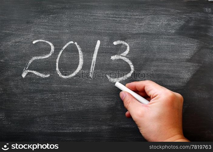 2013 written in chalk on a smudged blackboard,with a hand holding chalk