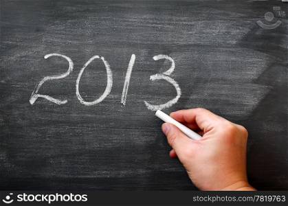 2013 written in chalk on a smudged blackboard,with a hand holding chalk
