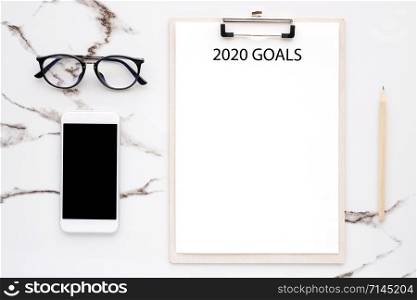 2020 goals on blank note paper with copy space for text and smart phone with blank screen on white marble background, new year aim to success in business background