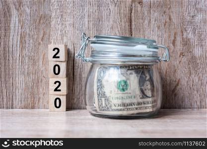 2020 Happy New Year with US dollar money glass American on wood table background. business, investment, retirement planning, finance, Saving and New Year Resolution concepts
