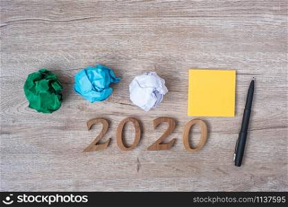 2020 Happy New year with yellow note, crumbled paper and pen on wooden table background. New You, Start, Idea, Creative, Innovation, Resolution and Goal concept