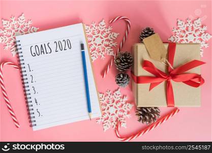 2020 New year concept. Goals 2020 list in notepad, gift box and christmas decoration on pink pastel color with copy space