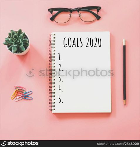 2020 New year concept. Goals list in notepad, smartphone, stationery on pink pastel color with copy space
