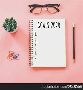 2020 New year concept. Goals list in notepad, smartphone, stationery on pink pastel color with copy space