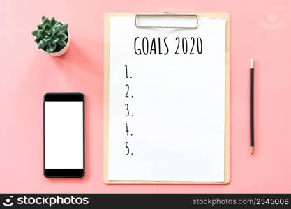 2020 New year concept. Goals list in stationery, blank clipboard, smartphone, pot plant on pink pastel color with copy space