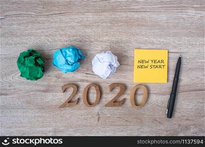 2020 NEW YEAR NEW START word on yellow note with pen and crumbled paper on wooden table background. RESOLUTION, Strategy and Goal concept
