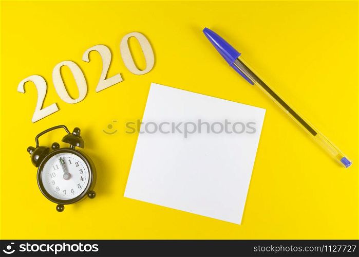 2020, paper, pen and black alarm clock on yellow background
