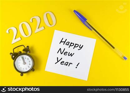 2020, paper with happy new year, pen and black alarm clock on yellow background