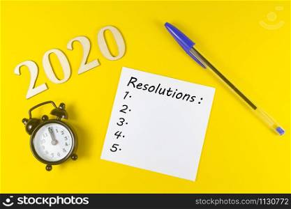 2020, paper with resolutions, pen and black alarm clock on yellow background