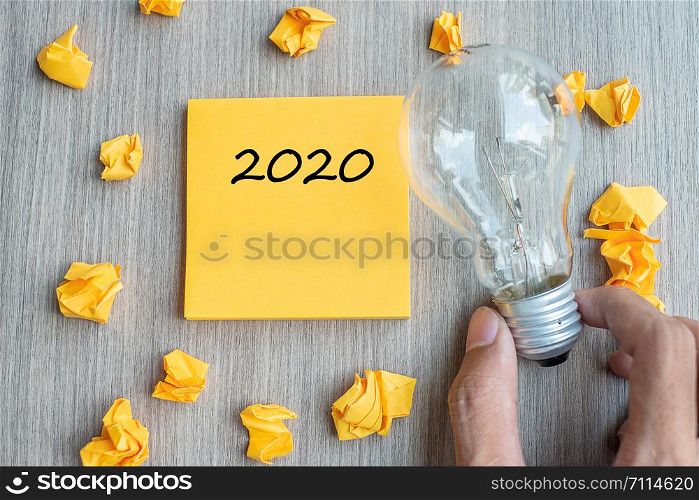 2020 words on yellow note and crumbled paper with Businessman holding lightbulb on wooden table background. New Year New Idea Creative, Innovation, Imagination, Resolution and Goal concept