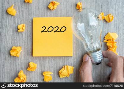 2020 words on yellow note and crumbled paper with Businessman holding lightbulb on wooden table background. New Year New Idea Creative, Innovation, Imagination, Resolution and Goal concept