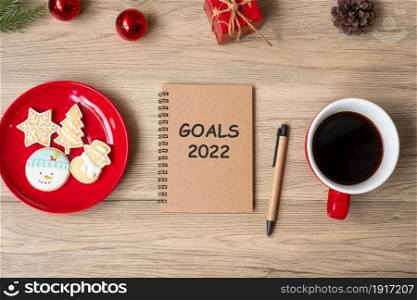 2022 GOAL with notebook, black coffee cup, Christmas cookies and pen on wood table. Xmas, Happy New Year, Resolution, To do list, Strategy and Plan concept