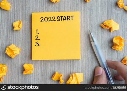 2022 Start word on yellow note with Businessman holding pen and crumbled paper on wooden table background. New Year, Resolutions, Strategy and Goal concept