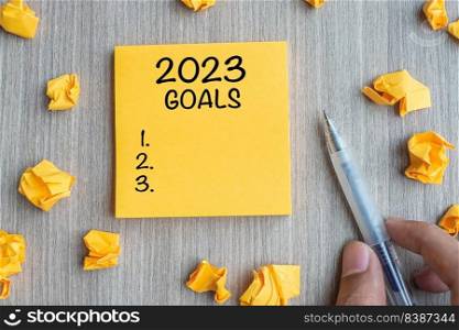 2023 Goal word on yellow note with Businessman holding pen and crumbled paper on wooden table background. New Year New Start, Resolutions, Strategy, mission concept