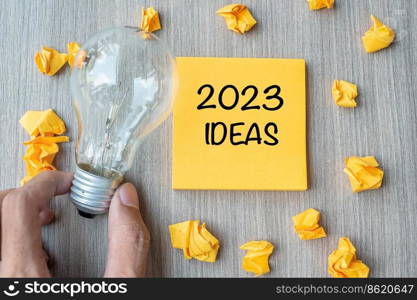 2023 Idea words on yellow note and crumbled paper with Businessman holding lightbulb on wooden table background. New Year New Start Creative, Innovation, Imagination, Resolution and Goal concept