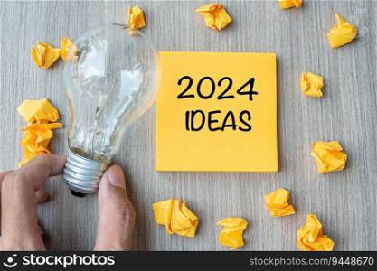 2024 Idea words on yellow note and crumbled paper with Businessman holding lightbulb on wooden table background. New Year New Start Creative, Innovation, Imagination, Resolution and Goal concept