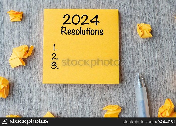 2024 RESOLUTIONS word on yellow note with pen and crumbled paper on wooden table background. New start, Strategy and Goal concept