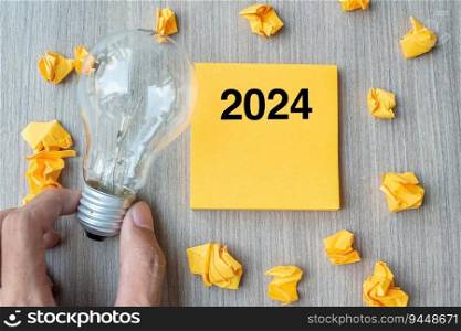 2024  words on yellow note and crumbled paper with Businessman holding lightbulb on wooden table background. New Year New Idea Creative, Innovation, Imagination, Resolution and Goal concept
